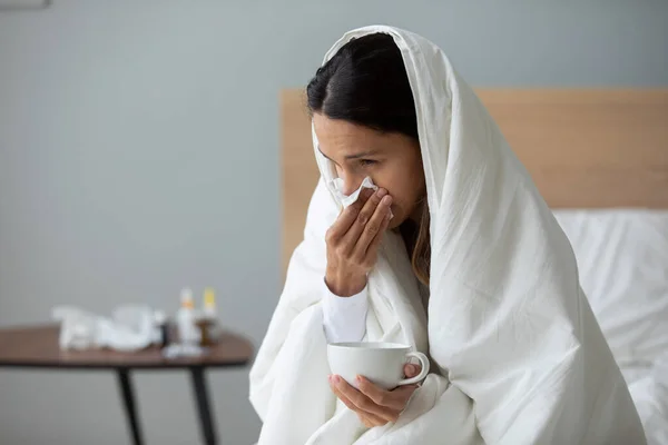 Woman holding cup with hot beverage and blows runny nose — Stock Photo, Image
