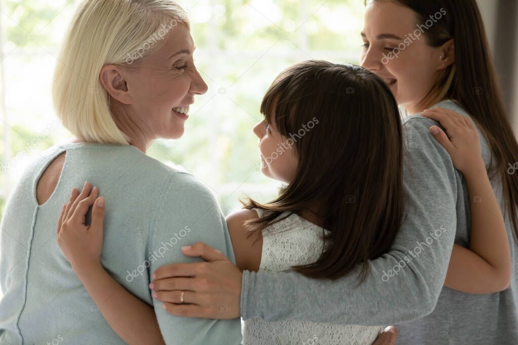 Rear view mother and grandmother embracing little granddaughter indoors