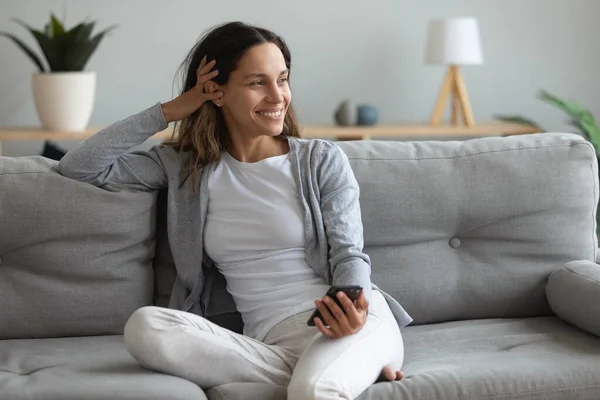 Beautiful woman spend lazy weekend seated on couch with smartphone — Stock Photo, Image