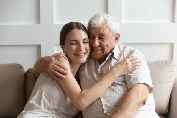 Caring adult young woman cuddling happy older hoary father.