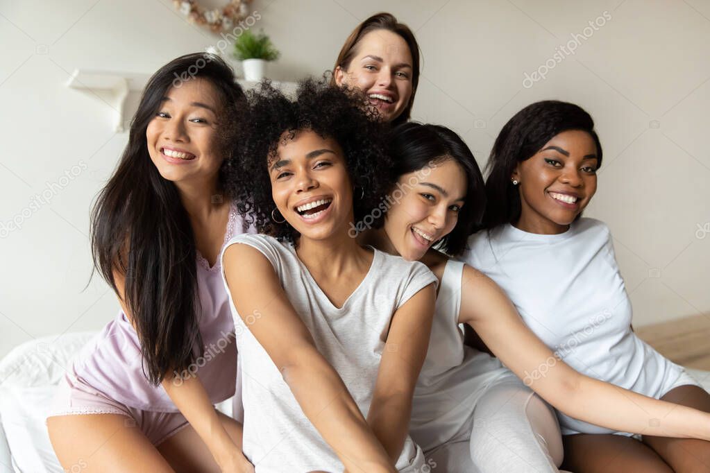 Five happy multiracial ladies wear sleepwear posing together on bed