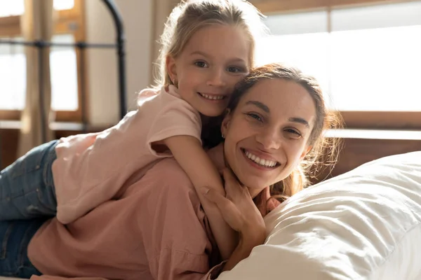 Little girl embracing mom lying on bed looking at camera — Stock Photo, Image