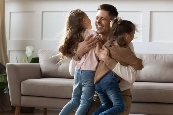 Веселий тато обіймає дітей дочок, які качаються вдома святкувати возз'єднання — стокове фото
