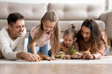 Mutlu ebeveynler ve çocuklar yerde dinozorlarla oynuyorlar.