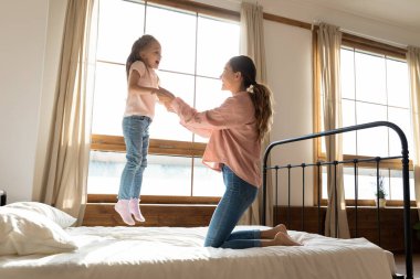 Sevimli küçük kız yatakta zıplayıp annesiyle oynuyor.