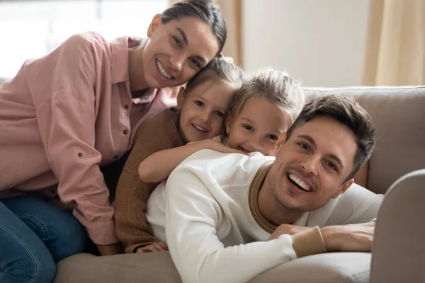 Счастливая семья из четырех человек сидит на диване и смотрит в камеру. — стоковое фото