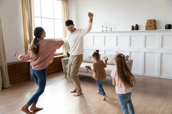 Vicces aktív szülők és gyerekek lányai táncolnak a nappaliban — Stock Fotó