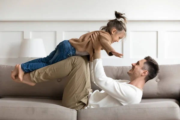 Щасливий батько піднімає милу доньку, яка грає на дивані — стокове фото