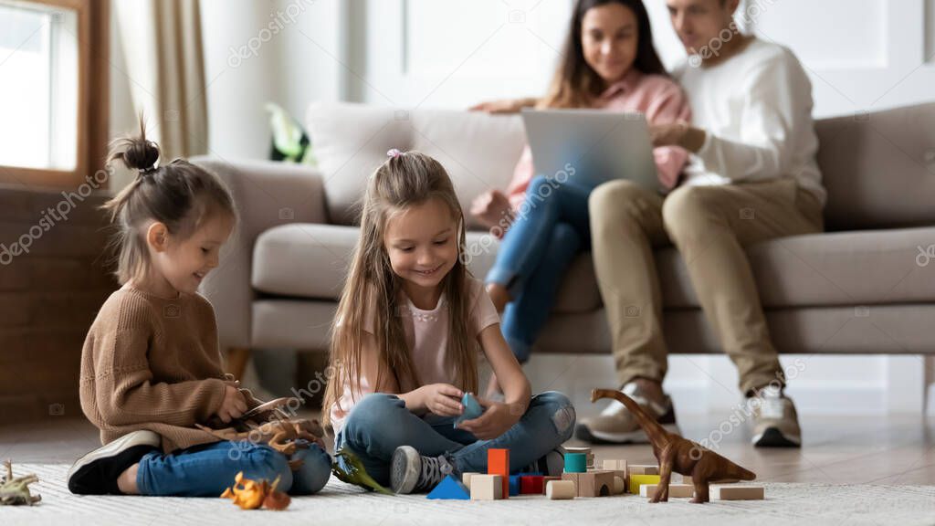 Happy kids playing while parents using laptop in living room