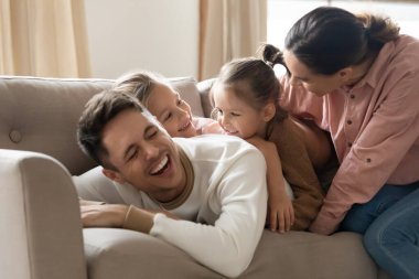 Neşeli ebeveynler kanepede uzanmış küçük kızlarıyla oynarken gülüyorlar.