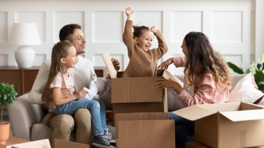 Mutlu ebeveynler ve çocuklar taşınma gününde kutuları açarak oynuyorlar.