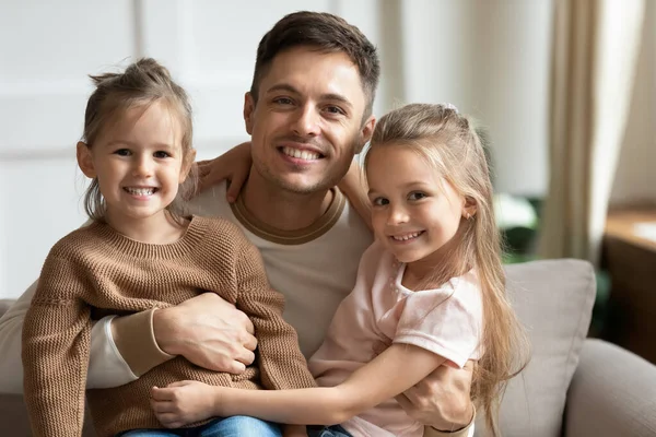 Gelukkig jong vader omarmen schattig kids dochters kijken naar camera — Stockfoto