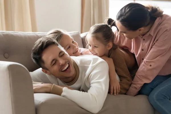 Vrolijke ouders lachen spelen met kleine dochters liggend op de bank — Stockfoto