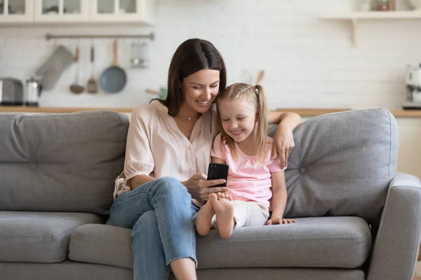 Щаслива мама і дочка насолоджуються за допомогою смартфона на дивані — стокове фото