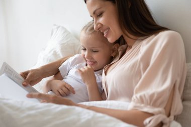 Bekar anne kucağı kızı yatakta kitap okuyor.