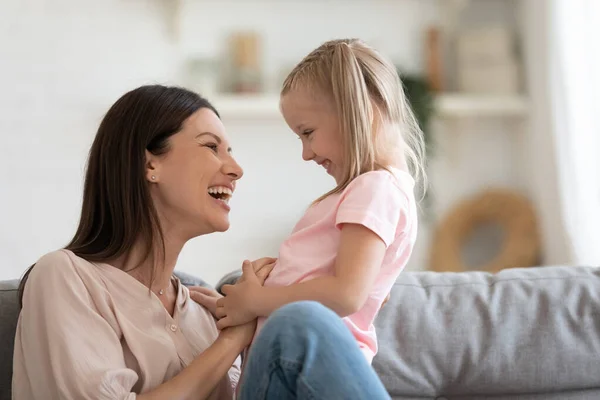Skrattande ung mamma kittling leka med barn dotter på soffan — Stockfoto