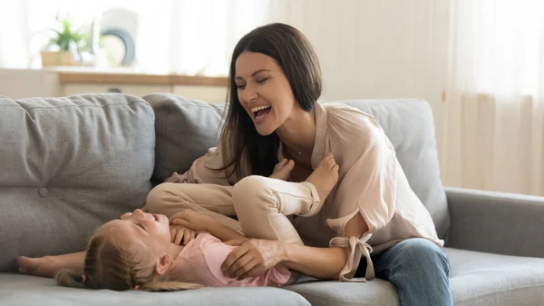 Alegre madre cosquillas lindo niño hija riendo jugando en sofá —  Fotos de Stock