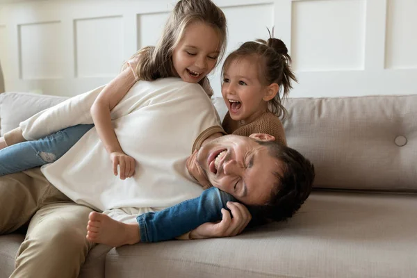 Funny young father playing with cute little children on sofa — Stock Photo, Image