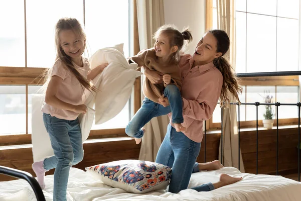 Happy mom and little daughters enjoying pillow fight on bed — Stock Photo, Image