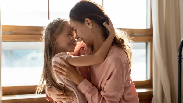 Cariñosa mamá y pequeña hija abrazando la vinculación en el dormitorio soleado —  Fotos de Stock