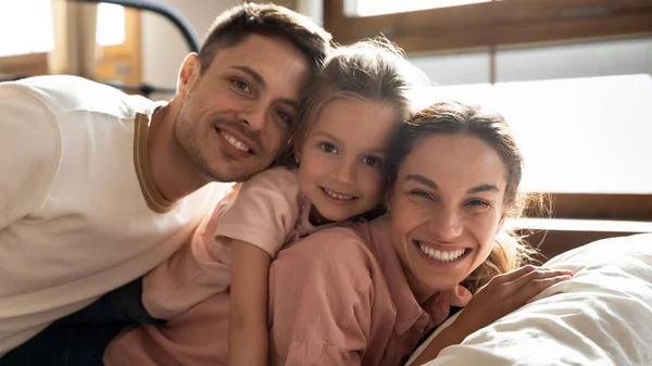 Padres felices e hija niño mirando a la cámara en la cama —  Fotos de Stock