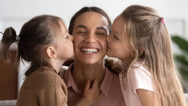 Two cute adorable little daughters kissing happy mum on cheeks — Stock Photo, Image