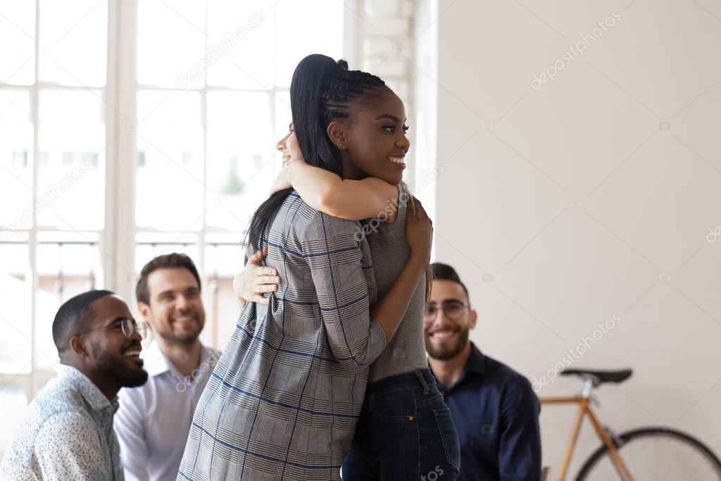 Happy african american manager hugging smiling female colleague.