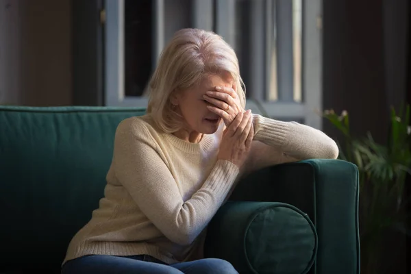 Elderly woman sitting on couch crying covered face with hand — Stock Photo, Image