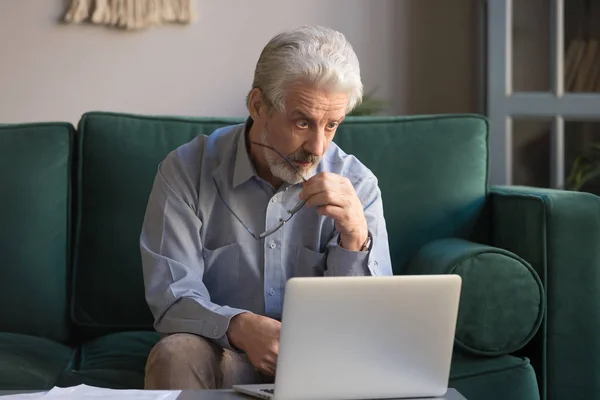 Hayretler içinde kalan yetişkin adam bilgisayar ekranına bakarken gözlüklerini çıkarıyor. — Stok fotoğraf