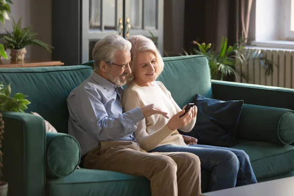 Elderly couple sitting on couch with smartphone discuss new application — Stock Photo, Image