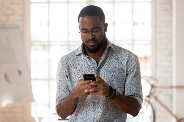 Ciddi bir Afrikalı Amerikalı genç çalışan akıllı telefon kullanıyor..