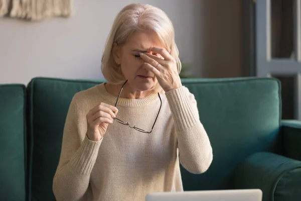 Пожилая женщина снимает очки устал от компьютерной работы — стоковое фото