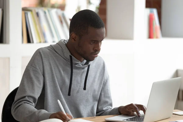 Серьезный чернокожий студент использует ноутбук, занят учебой . — стоковое фото