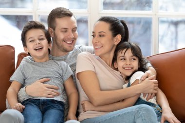 Anaokulu çocuklarıyla kanepeye uzanmış mutlu bir aile.