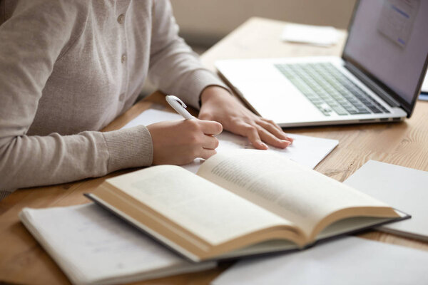 Close up female student writing down notes from opened textbook.