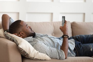 Milenyum melezi bir adam rahat koltukta cep telefonu kullanıyor.