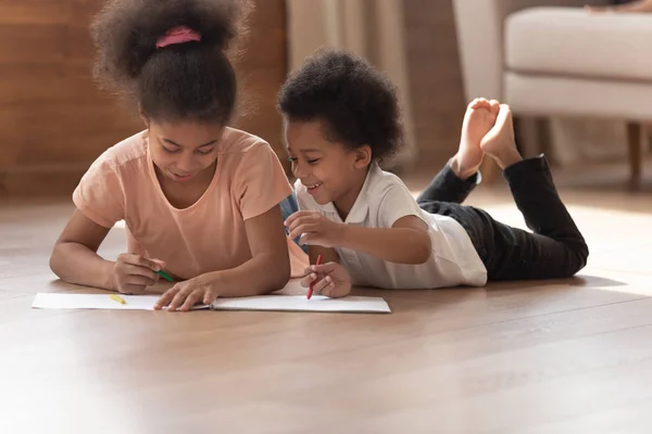 Afrikaanse kleine kinderen tekening liggend op warme vloer thuis — Stockfoto
