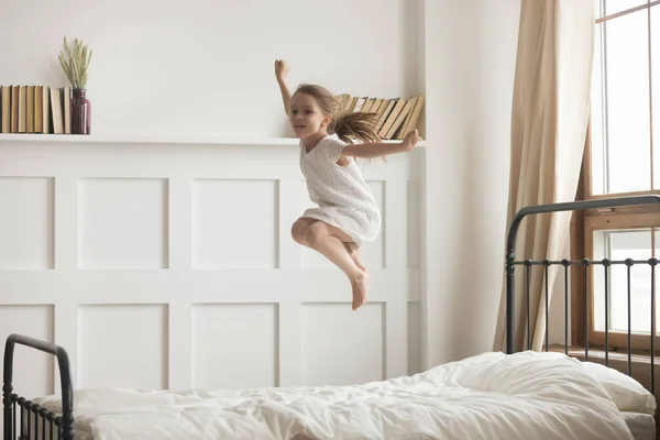 Happy anak perempuan prasekolah melompat tinggi santai di kamar tidur — Stok Foto