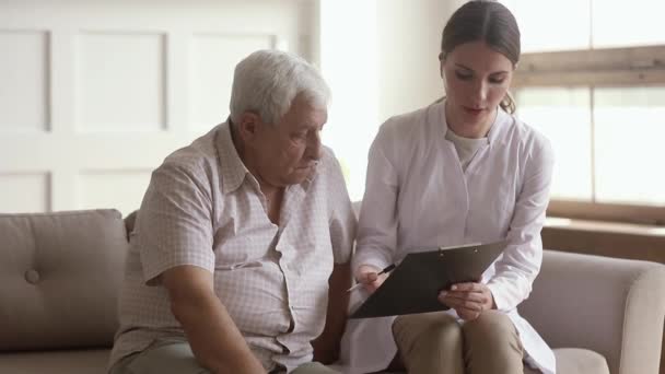Молодая медсестра сиделка держит планшет консультируя пожилого человека — стоковое видео