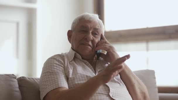 Счастливый старший мужчина держит сотовый телефон разговаривая по телефону дома — стоковое видео
