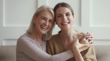 Gülümseyen olgun bir anne genç yetişkin bir kızı kucaklıyor, portre