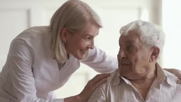 Улыбающаяся взрослая добрая медсестра разговаривает со стариком-инвалидом — стоковое видео