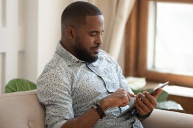 Afro-Amerikalı adam evde tablet kullanarak dinleniyor.