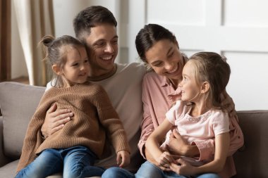 Çocukları kucağında tutan mutlu ebeveynler koltukta rahatlar.