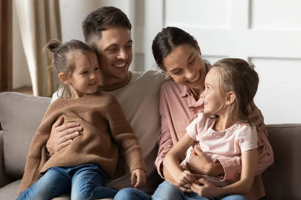 Glücklich liebende Eltern, die ihre Kinder auf dem Schoß halten, entspannen sich auf der Couch — Stockfoto