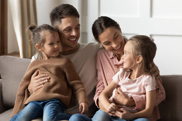 Счастливые любящие родители держат детей на коленях расслабиться на диване
