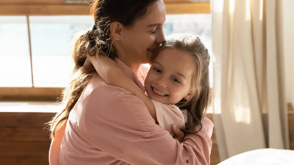En omtenksom, ung mor som klemmer en søt, liten datter hjemme – stockfoto