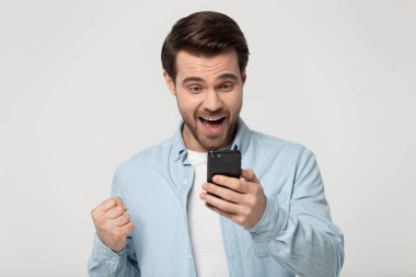 Neşeli genç adam cep telefonundan iyi bir mesaj aldığı için heyecanlanıyor.