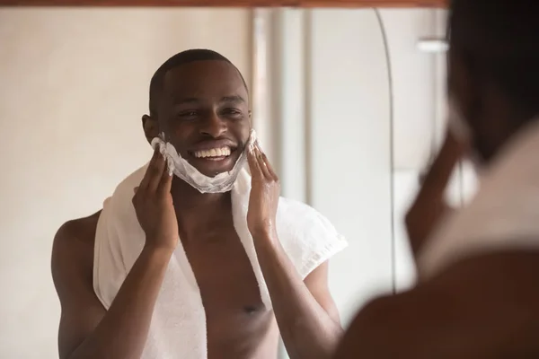 African American man look in mirror shaving in bathroom — Stock Photo, Image