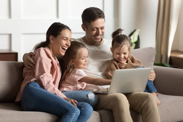 Позитивные родители и дети дочери смеются, используя ноутбук дома — стоковое фото
